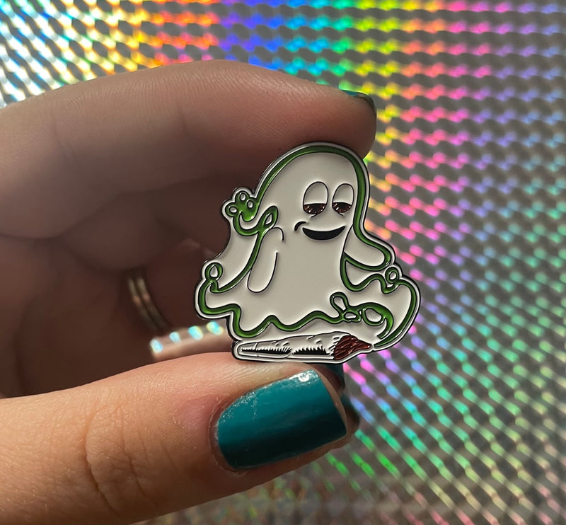 Ghost themed enamel pin is held in front of a holographic background