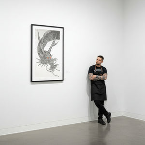 Man standing next to a framed artwork of a dragon on a white wall