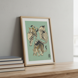Framed artwork of three stylized cats on a light green background, leaning against a white wall.